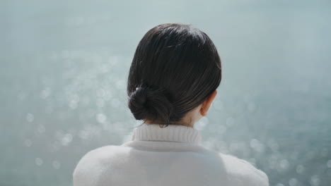 Woman-tourist-listening-music-in-wireless-earbuds-sitting-at-lake-water-close-up
