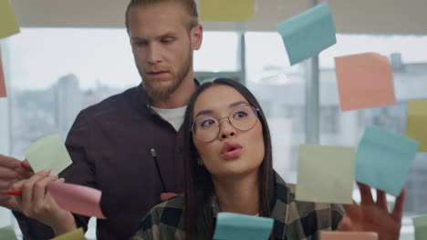 Eyeglasses-creator-writing-sticker-wall-at-office-close-up.-Woman-talking-to-man