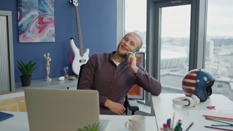 Hombre-Sonriente-Charlando-Con-El-Primer-Plano-De-La-Oficina-Del-Teléfono-Inteligente.-Feliz-Emprendedor-Viendo-La-Computadora-Portátil