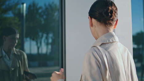 Woman-looking-reflection-window-taking-off-wireless-headphones-outdoors.