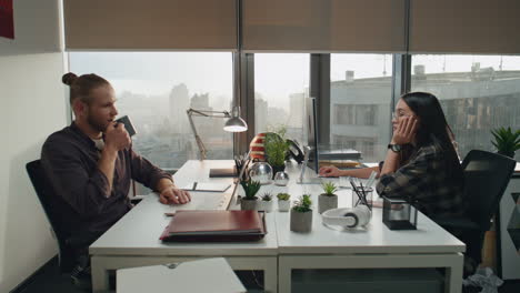 Pareja-De-Negocios-Trabajando-Hasta-Tarde-En-El-Cierre-De-La-Agencia.-Hombre-Descansando-Mujer-Comunicando