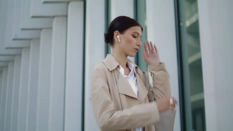 Mujer-Hablando-Con-Auriculares-Inalámbricos-De-Pie-Cerca-Del-Edificio-Moderno-De-La-Ciudad-De-Cerca.