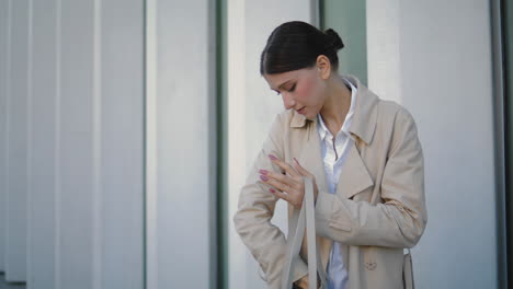 Businesswoman-looking-phone-bag-near-building.-Girl-taking-smartphone-vertically