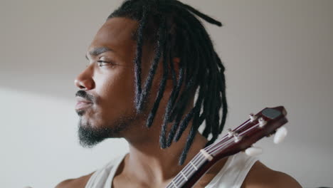 Thoughtful-guy-enjoying-ukulele-at-apartment-closeup.-Involved-man-playing-song