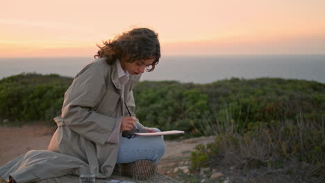 Inspired-girl-painting-evening-ocean-vertical.-Focused-artist-relax-rocky-hill