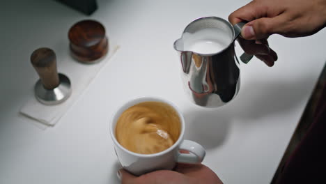 Barista-pouring-milk-coffee-from-pitcher-close-up.-Process-preparing-cappuccino.