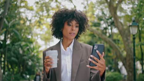 Woman-talking-phone-video-call-walking-city-park-hold-paper-coffee-cup-closeup.