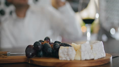 Delicious-cheese-appetizers-lying-on-board-vertically-closeup.-Man-taking-grapes