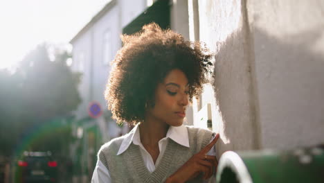 Model-posing-leaning-wall-at-summer-sunlight-close-up.-Woman-standing-on-street.