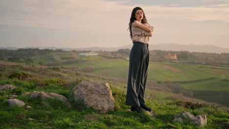 Pensive-young-woman-posing-at-valley-in-front-cloudy-sky.-Girl-standing-on-grass