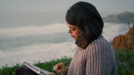 Mujer-Dibujando-La-Naturaleza-Nublada-En-El-álbum-Sentada-Sola-En-La-Playa-De-Noche-De-Cerca.