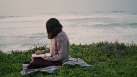 Woman-sitting-seashore-blanket-reading-book-at-dramatic-sea-view.-Girl-resting.