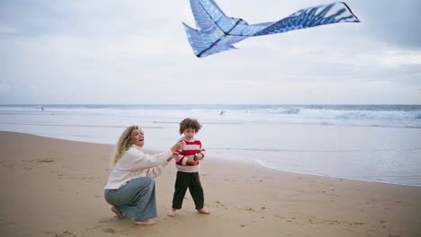 Niño-Alegre-Jugando-Cometa-Con-Su-Madre-En-La-Playa.-Padre-Joven-Cariñoso-Ayudando-A-Su-Hijo