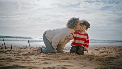 Mamá-Joven-Besando-A-Un-Niño-En-Vacaciones-De-Fin-De-Semana.-Padres-Felices-Construyendo-Castillos-De-Arena