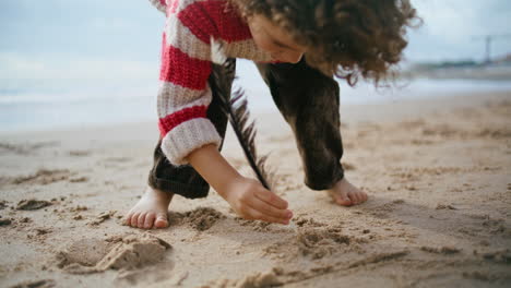 Little-boy-drawing-sand-with-bird-feather-closeup.-Focused-kid-resting-beach