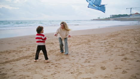 Niño-Intentando-Lanzar-Cometas-Con-Mamá-En-Una-Playa-Ventosa.-Madre-Emocionada-Ayudando-A-Su-Hijo