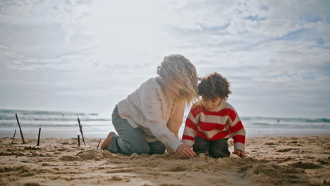 Mutter-Entspannt-Sich-Am-Herbststrand-Mit-Kleinem-Sohn.-Sorglose-Familie-Baut-Sand