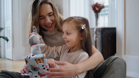 Curioso-Bebé-Abriendo-Regalo-En-Casa-De-Año-Nuevo.-Mamá-Presentando-Juguete-A-Hija