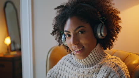 Headphones-lady-smiling-camera-armchair-portrait.-African-woman-enjoying-music