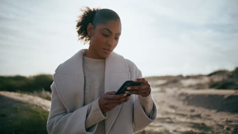 Calm-girl-message-smartphone-in-sunlight.-Serene-african-american-tourist-check
