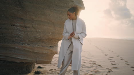 Woman-writing-beach-sand-at-shore-cliff-rock.-Black-hair-tourist-resting-ocean