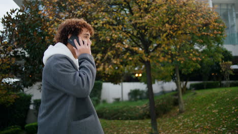 Lockiger-Teenager-Ruft-Telefon-Auf-Der-Straße-An,-Nahaufnahme.-Junger-Mann-Geht-Treppen-Im-Herbstpark