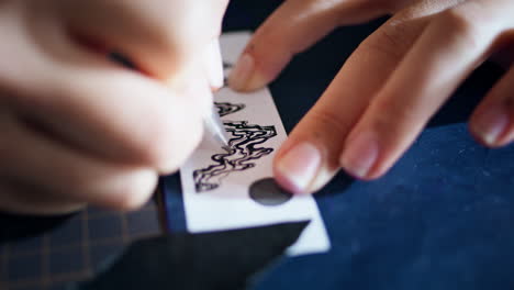 Tattooist-hands-transferring-sketch-at-table-closeup.-Woman-fingers-drawing-pen