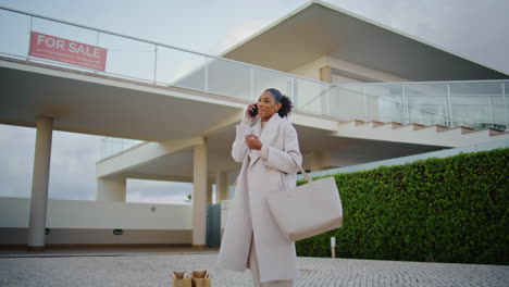 Happy-realtor-talking-phone-at-modern-mansion.-Smiling-african-american-buyer