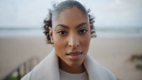 Portrait-serene-african-american-woman-look-camera-at-blurred-ocean-background.