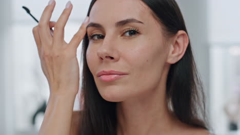 Satisfied-model-applying-mascara-indoor-mirror-pov-portrait.-Lady-makeup-routine