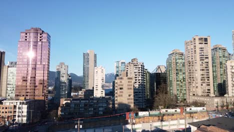 aerial-rise-dolly-roll-over-downtown-high-rises-overlooking-a-development-property-at-Nicola-and-Robson-as-the-sun-mirrors-the-reflection-on-a-pink-glass-residential-condominium-tower-in-vancouver-CA