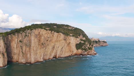 Gorgeous-scenic-flight-by-Montagna-Spaccata-promontory-sheer-vertical-cliff-wall-to-reveal-castle-on-rocky-summit,-Italy,-sideways-aerial