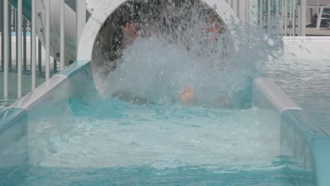 A-little-girl-laughs-as-she-slides-out-the-bottom-of-a-tube-slide-at-a-waterpark