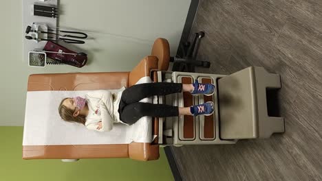 Vertical-video:Portrait-of-child-sitting-on-chair-in-waiting-area-at-facility