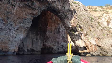 Traditional-Maltese-luzzu-tourist-boat-approaching-Blue-Grotto-rocky-coastline-caves-in-Malta-on-a-sunny-summer-day