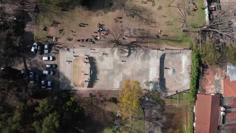 Drone-descending-towards-urban-skate-park-in-the-outdoors-with-people-using-it