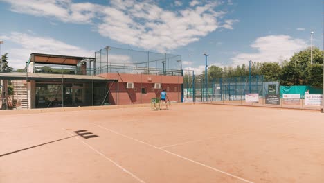 Tennis-woman-with-racket-pull-ball-cart-and-leave,-dolly-in-slow-motion