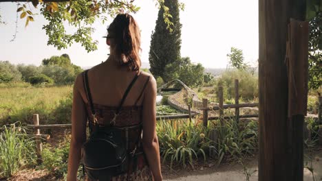 Woman-discovers-the-garden-and-pond-of-perfumery-museum-in-summer,-back-rear-view