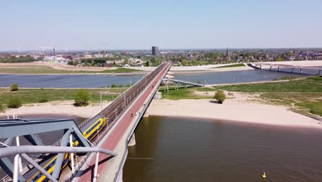 El-Tren-Pasa-Por-El-Puente-Y-El-Río-Waal-En-Nijmegen,-Gelderland,-Países-Bajos---Antena