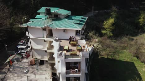 Aerial-drone-backward-moving-shot-of-a-group-of-friends-on-the-rooftop-of-hotel-while-on-a-trip-to-Kasol,-Himachal-Pradesh,-India-at-daytime