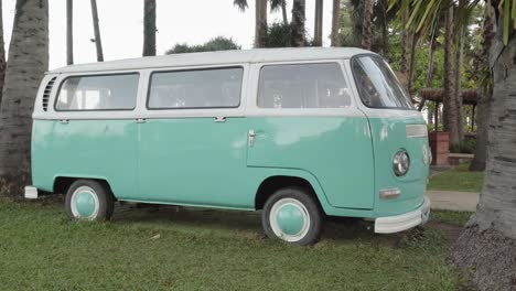 A-pan-reveal-shot-of-a-classic-two-tone-VW-Bus-parked-between-two-coconut-trees,-a-perfect-setting-for-a-retro-hippy-carefree-lifestyle,-Pattaya,-Thailand