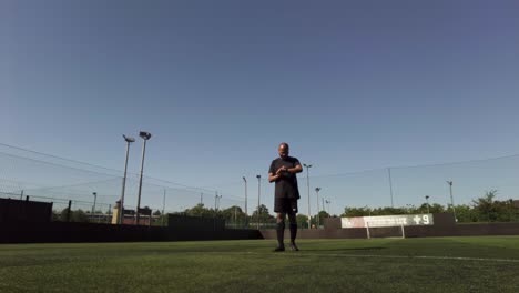 Bald-Ethnic-Minority-Male-Warming-Up-On-Football-Pitch-By-Stretching-Legs-On-Clear-Sunny-Day