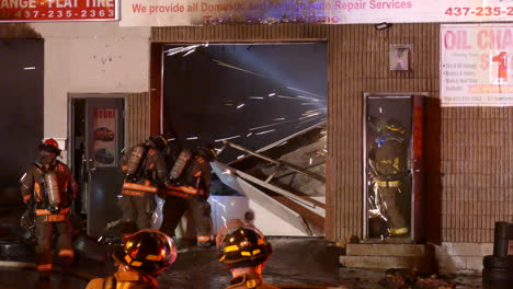 Team-of-firefighters-work-at-night-in-the-ruins-of-a-building-with-a-metal-grinder-that-emits-sparks