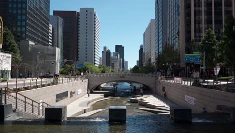 Vista-Elevada-Del-Agua-De-La-Cascada-Cheonggyecheon-Cayendo-En-El-Arroyo-Con-Multitud-De-Personas-Relajándose-En-Verano