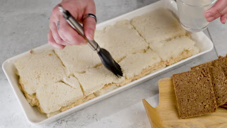 Static-Shot-Of-An-Individual-Using-A-Culinary-Brush-To-Put-A-Wash-Over-The-Slices-Of-Bread-Preparing-Them-For-The-Next-Stage