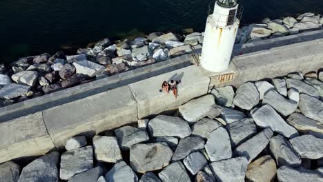 Paar-Sitzt-Neben-Dem-Alten-Leuchtturm-In-Camogli-Shore,-Blue-Seascape,-Genua