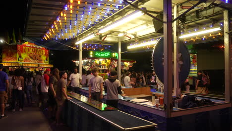 Las-Luces-De-Neón-Parpadean-Mientras-La-Gente-Juega-Juegos-De-Carnaval-En-Una-Noche-Oscura-En-La-Feria