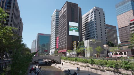 Lleno-De-Turistas-Parque-Del-Arroyo-Cheonggyecheon,-La-Gente-Cruza-El-Puente-Gwangtong-Viajando-En-Un-Hermoso-Día-De-Verano-En-El-Centro-De-La-Ciudad-De-Seúl,-Corea-Del-Sur