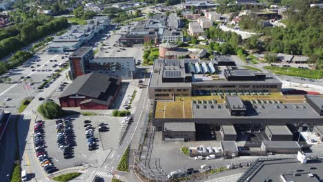 Asane-center-shopping-malls-besides-Asane-hall-and-Asane-church-outside-Bergen---Aerial-flying-over-street-looking-towards-mall-buildings-and-highway-e39-in-background