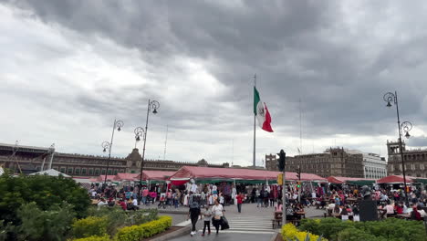 Toma-En-Cámara-Lenta-De-La-Bandera-De-México-Ondeando-Con-La-Vista-Completa-Del-Zócalo-En-El-Fondo-Al-Atardecer